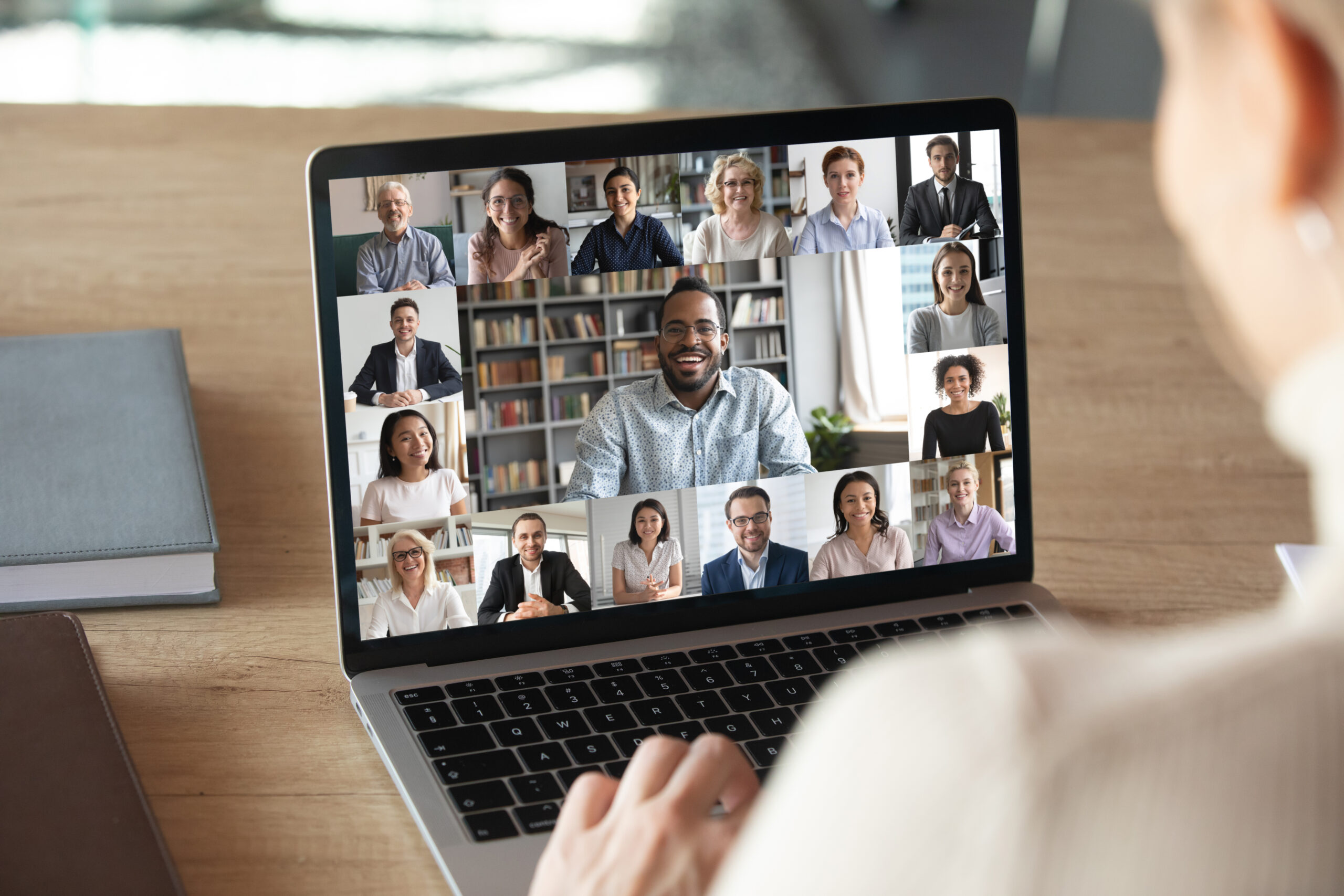 Back,View,Of,Female,Employee,Speak,Talk,On,Video,Call a person sitting with a laptop on their lap with a video call on the screen with several people