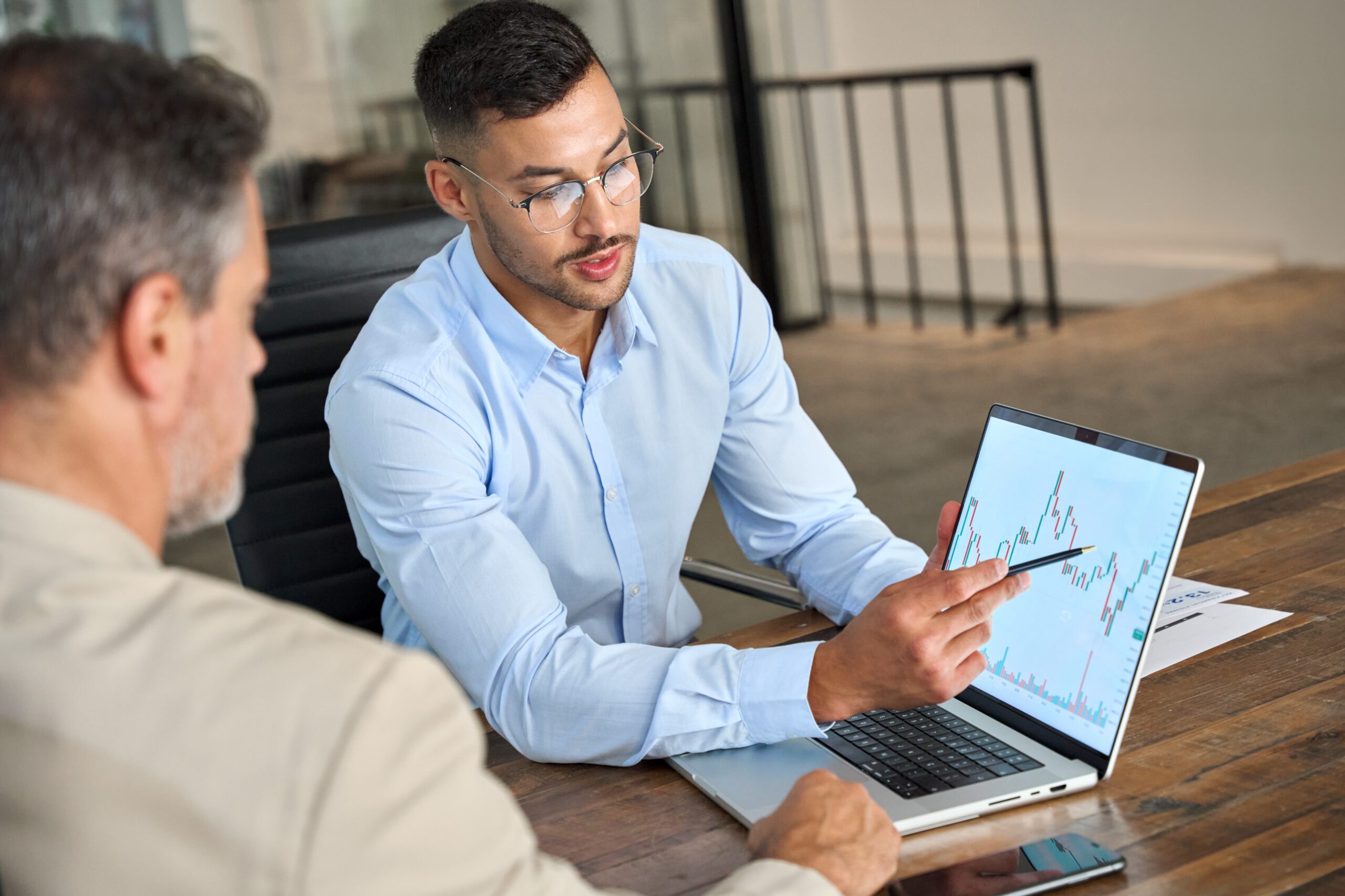 Financial,Advisor,Explaining,Invest,Stock,Market,Data,Consulting,Investor.,Two A person pointing to a grpah on a laptotp screen to show someone else next to them a specific data point