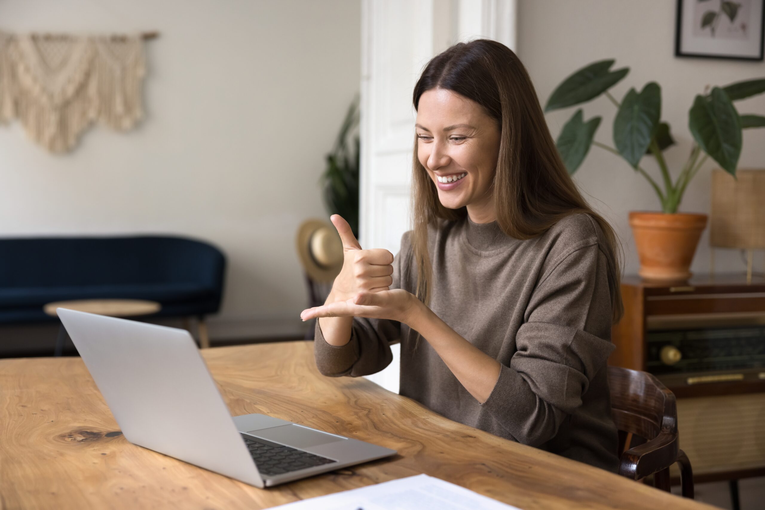 Young,Woman,Interacting,Remotely,Using,Laptop,,Video,Call,Application,And a person sitting at a table with a laptop on it as they use sign language to communicate